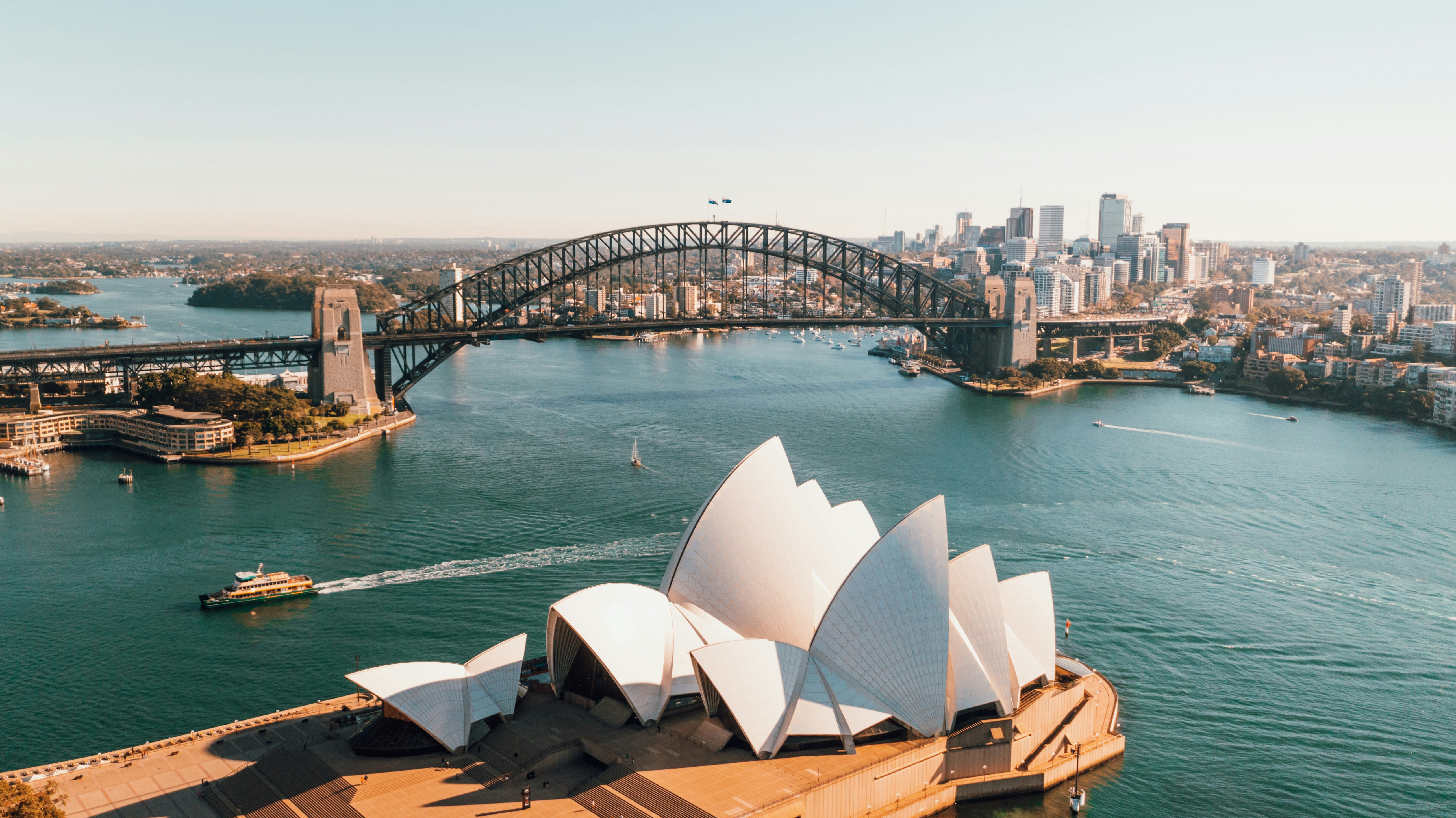 Aerial view of the Sydney Opera House with the Sydney Harbour Bridge and city skyline in the background.